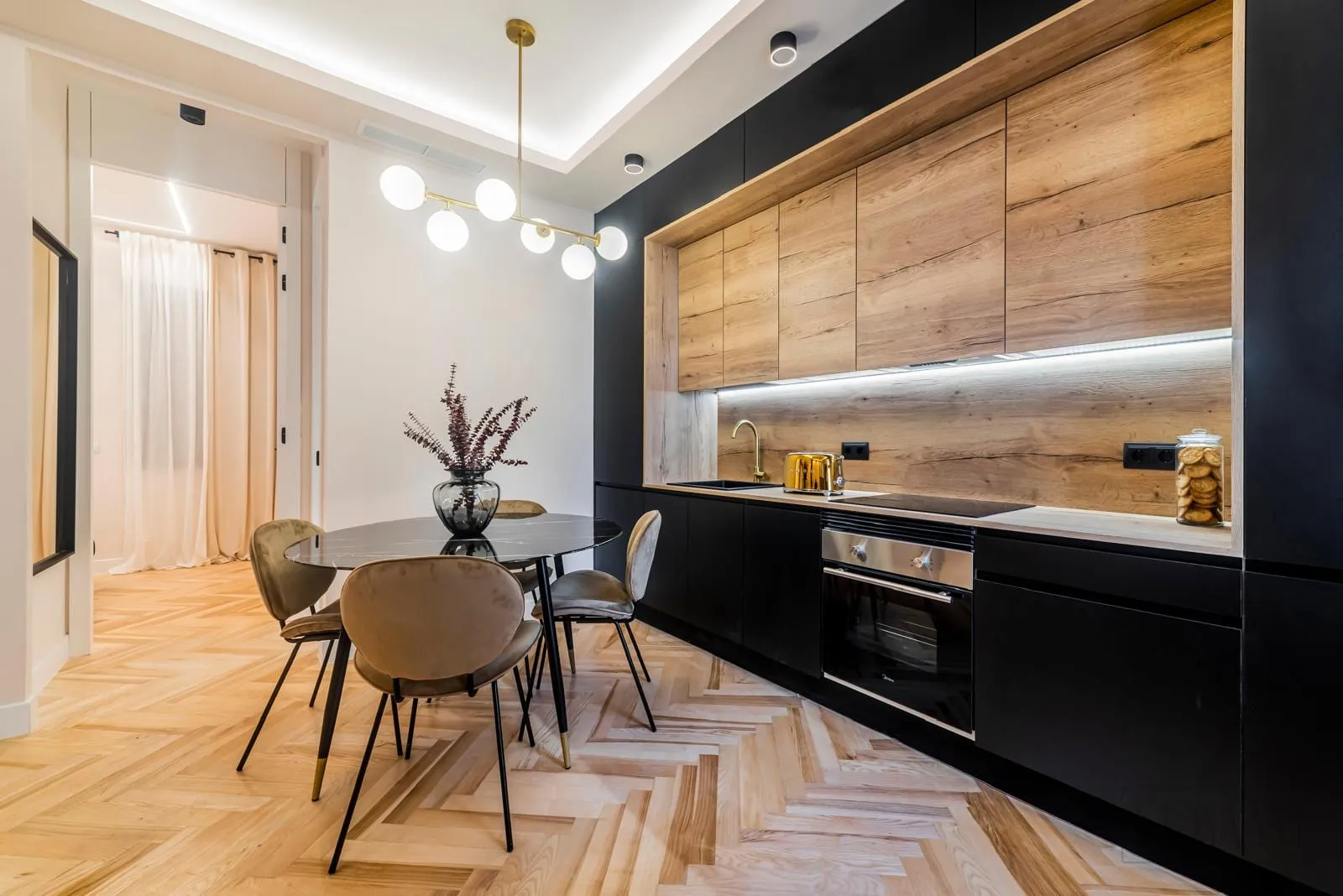 Cocina en negro y madera abierta al comedor, con mesa de mármol negro y suelo de roble en espiga.