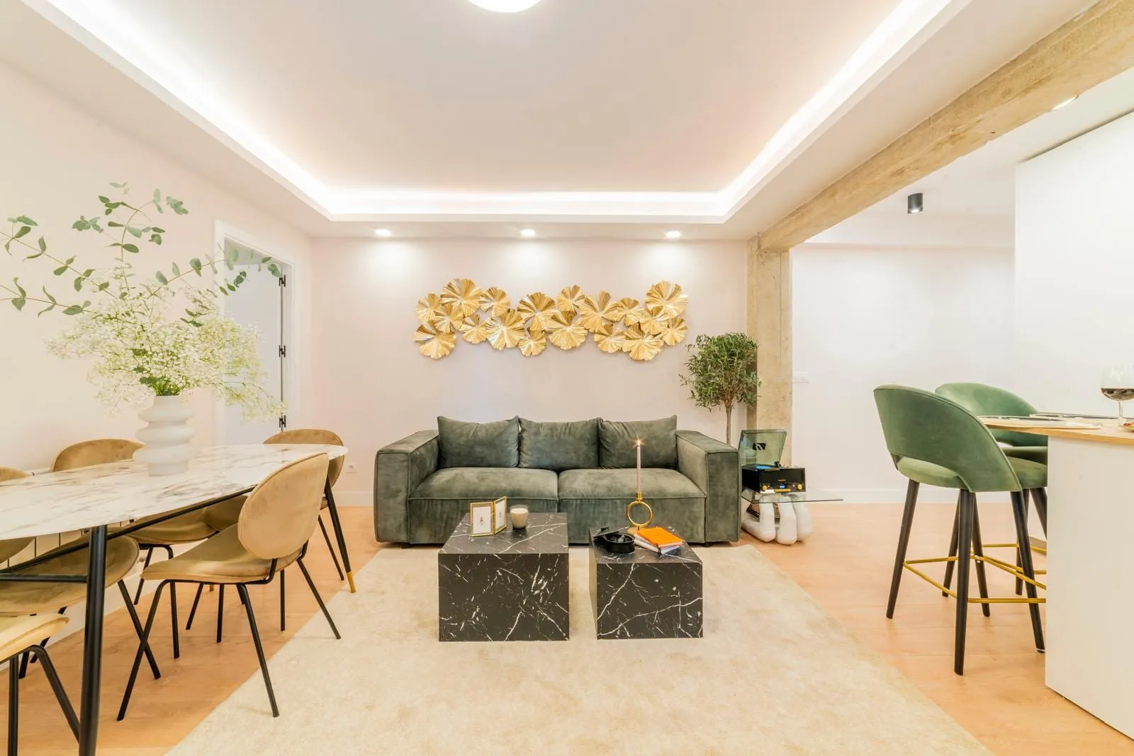 Salón comedor con sofá verde, mesa de mármol y techo con luz indirecta.